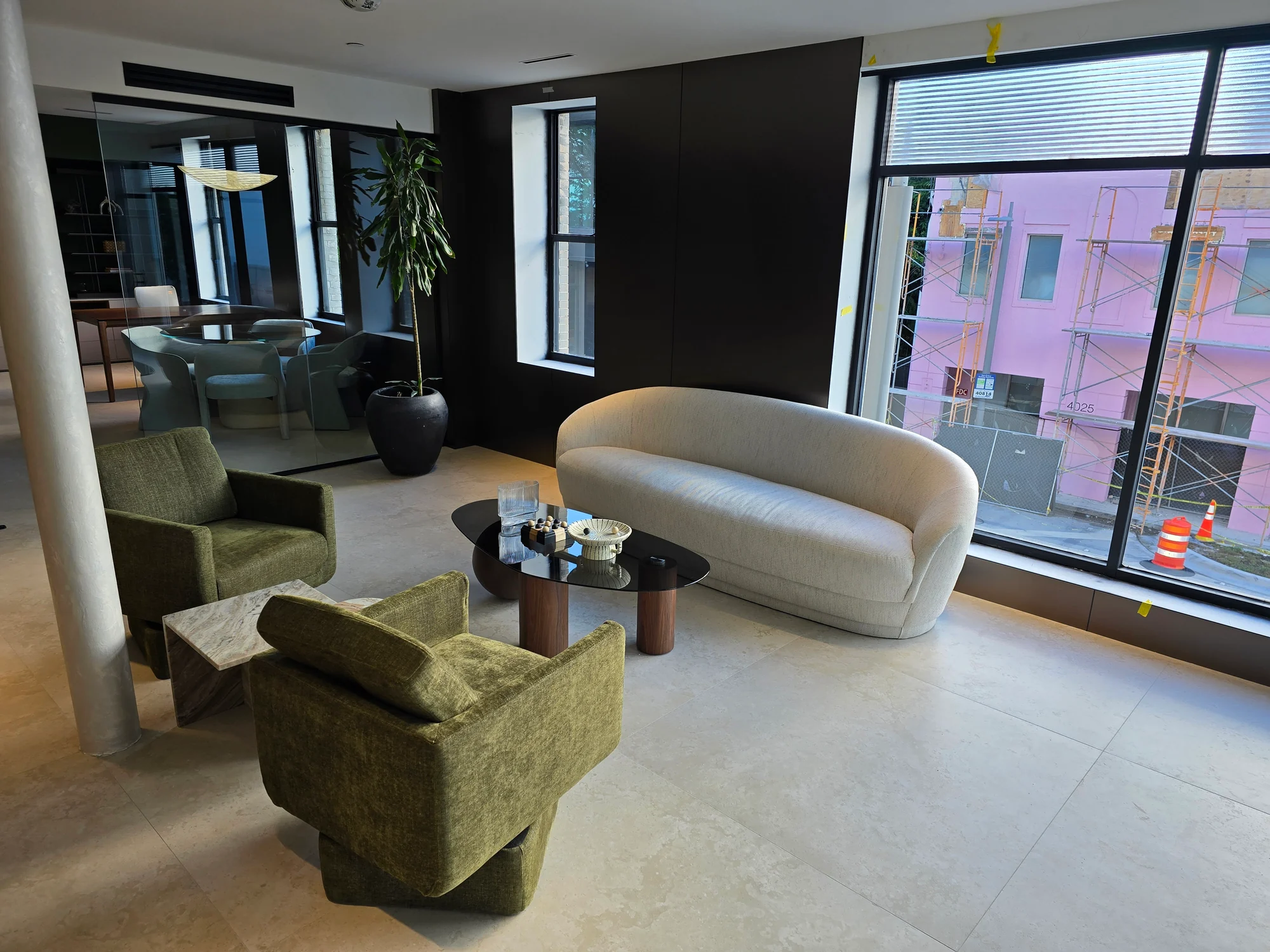 A cream sofa and green armchairs around a low table beside large windows.